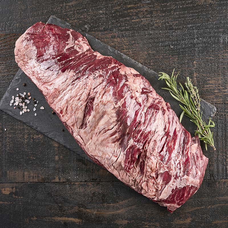 A large bavette cut, so large it overhands the black stone platter it sits on, surrounded by fresh herbs and spices.