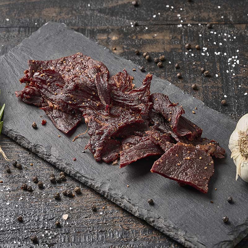Dried beef slices on a slate board with herbs and spices on a wooden surface