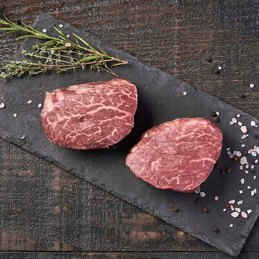 Two beautifully marbled filet mignon steaks from Yolo 8 Meats on a black stone platter, surrounded by rock salt and fresh herbs.