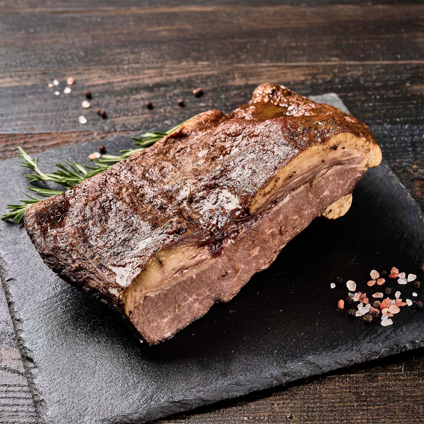 A large smoked brisket on a stone platter with fresh herbs and spices