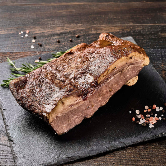 A large smoked brisket on a stone platter with fresh herbs and spices