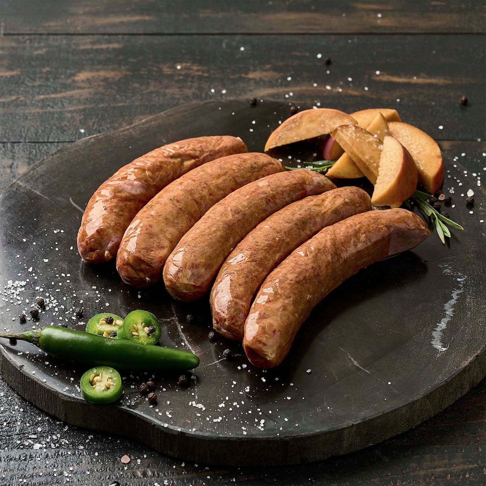 Five sausages on a dark stone plate with jalapeño on a wooden background