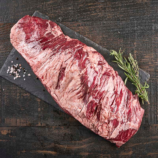 A large bavette cut, so large it overhands the black stone platter it sits on, surrounded by fresh herbs and spices.