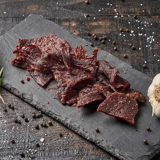 Dried beef slices on a slate board with herbs and spices on a wooden surface